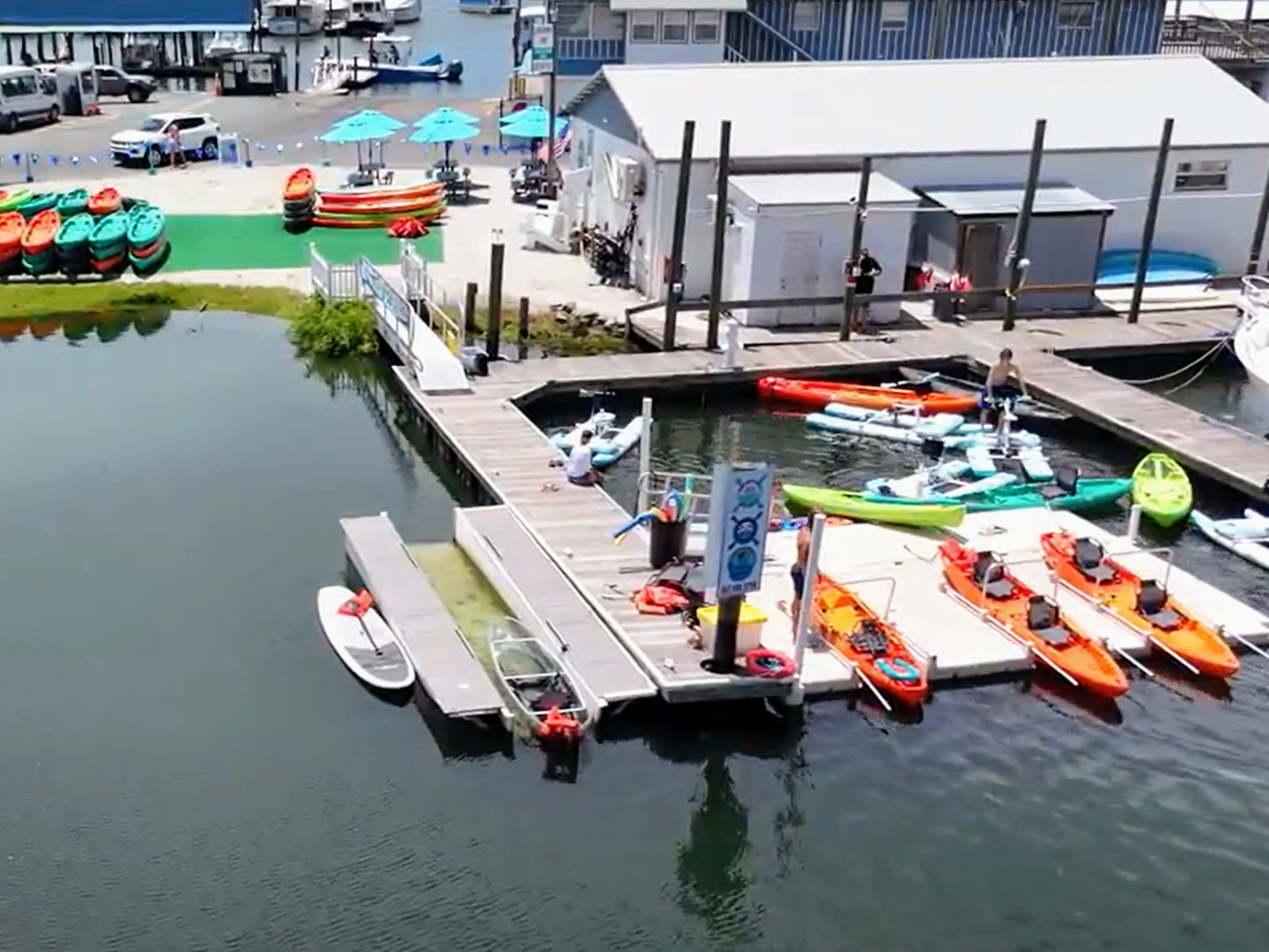 Aerial view of a dock with kayaks and paddleboards, adjacent to a boathouse and parked vehicles.